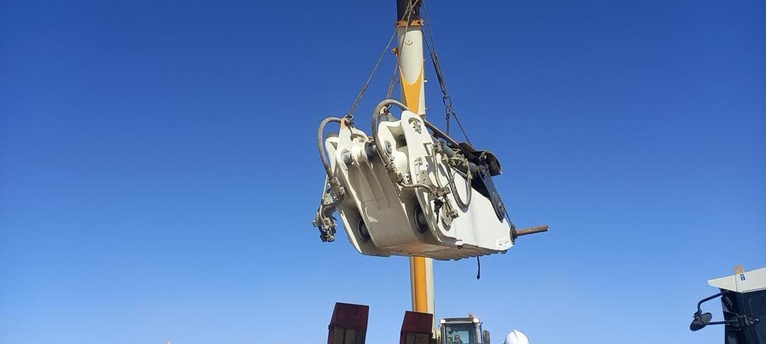 Heavy equipment attachment lifted by crane against a clear blue sky